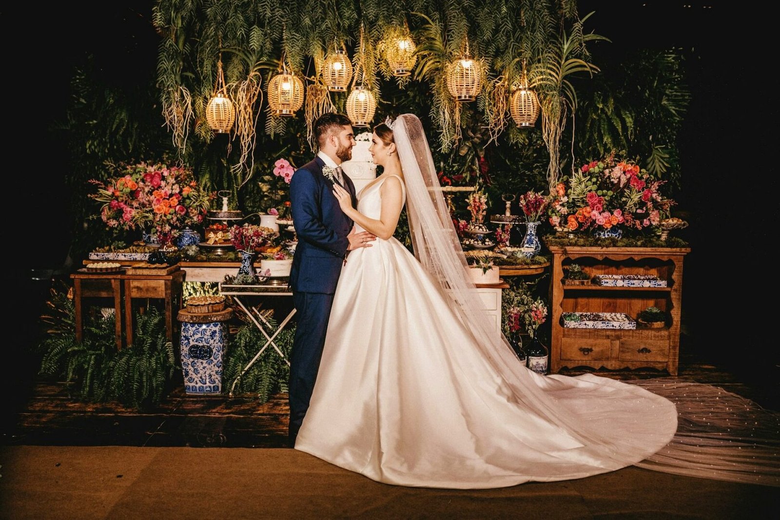 Pareja de novios en una escenografía rústica con luz cálida, rodeados de flores y helechos