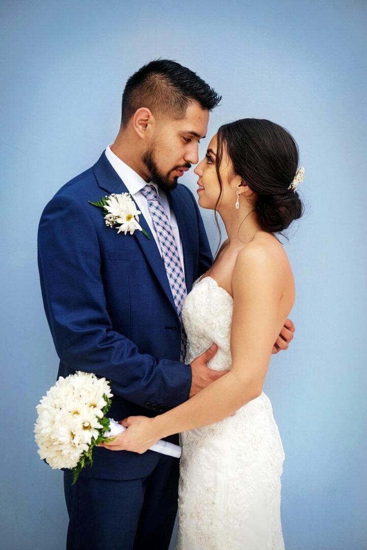 Novia sonriente entre los brazos de su esposo, con ramo blanco en estudio profesional de fotografía